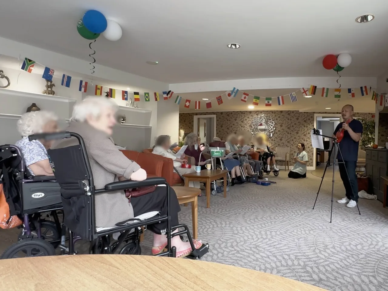 Large group HappierMusic sing-along session with elderly residents actively participating — care home music wellbeing programme, North London