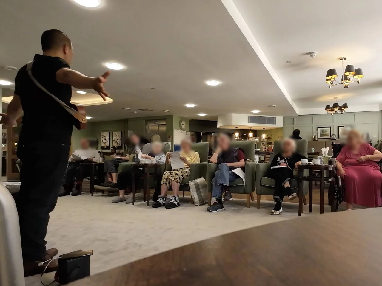 Elderly care home residents enjoying a live HappierMusic session with songbooks — familiar songs, live ukulele, Enfield and Hertfordshire care homes