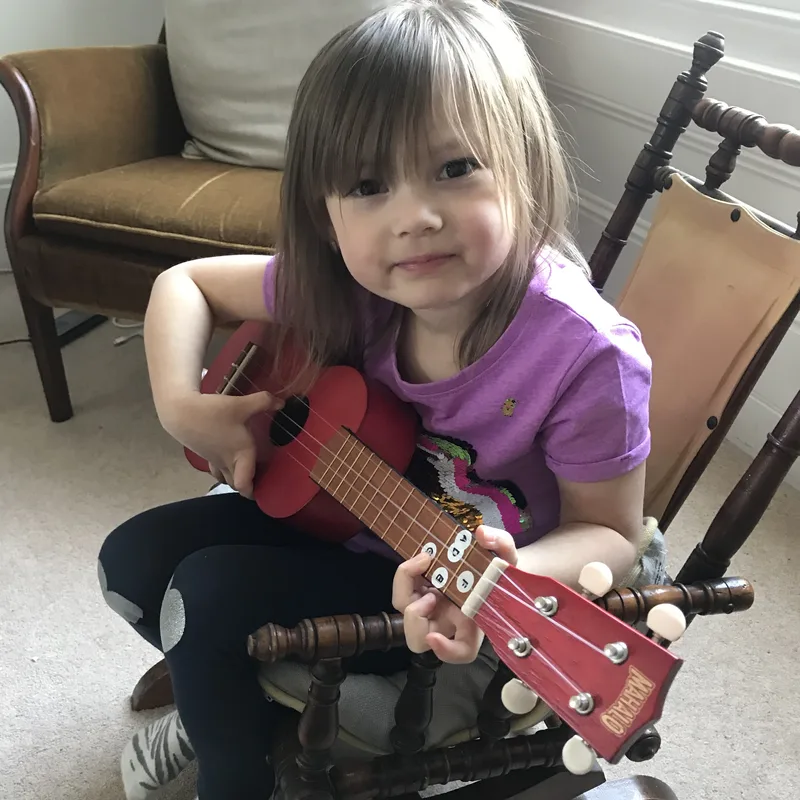 Young girl holding a red ukulele, smiling