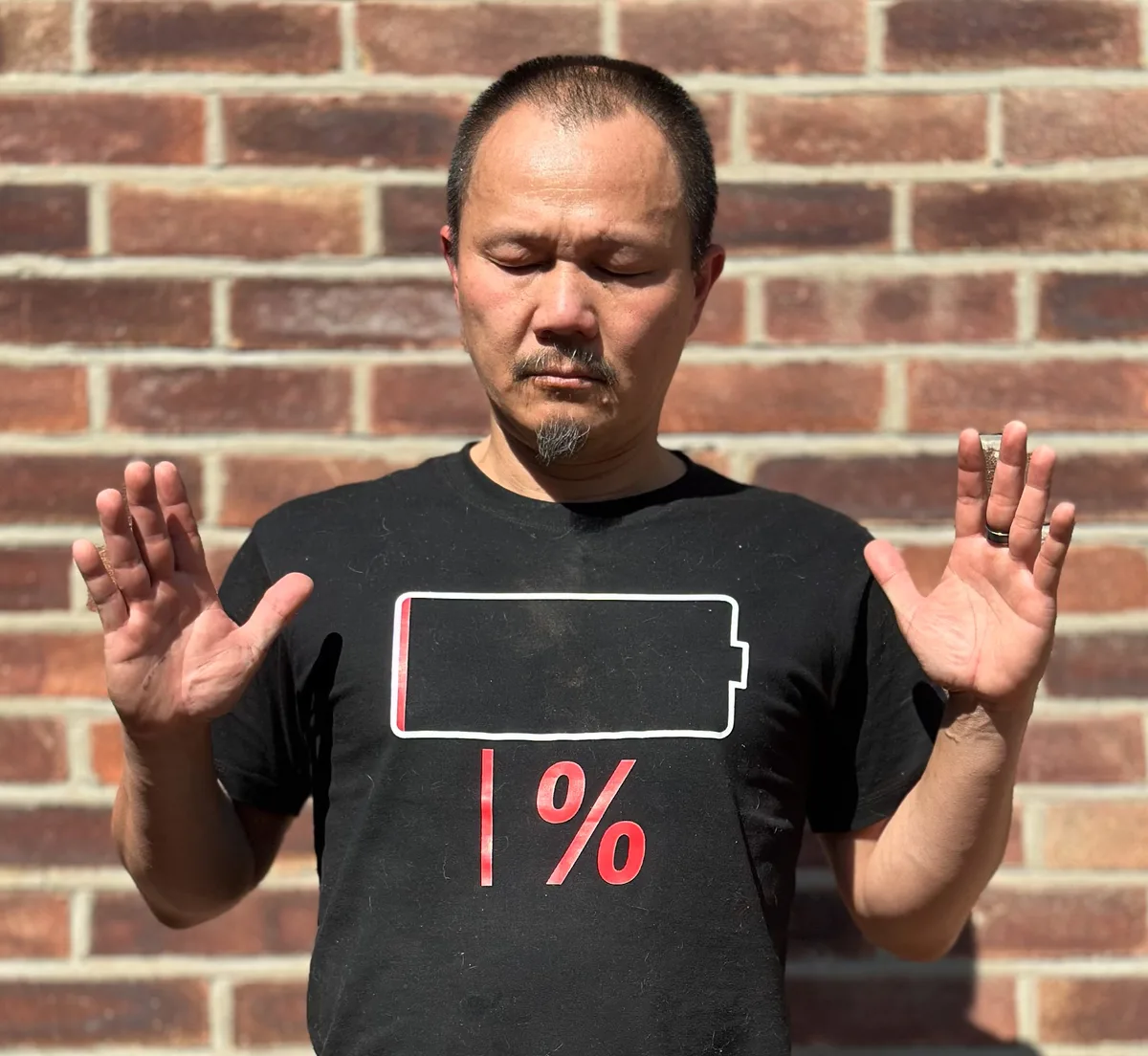 Frven Lim meditating with eyes closed wearing a 1 percent battery t-shirt, representing emotional exhaustion and the need for recharging
