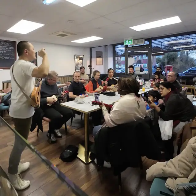 Children and adults playing ukulele together in a workshop